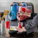 A person pouring a red drink into a Vollrath dual frozen beverage machine.