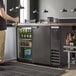 A man standing at a black bar with a Beverage-Air back bar refrigerator full of bottles.