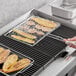 A person grilling food in an Outset Chrome Flex Grill Basket.