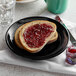 A Tuxton Concentrix black china plate with a piece of bread with jam on it.