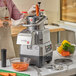 A man in a kitchen using an AvaMix Goliath food processor to shred carrots.