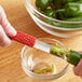 A person using an Outset stainless steel jalapeno corer with a red handle to core a green pepper.