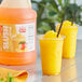 A plastic cup with a straw next to a slushy made from Carnival King Mango Slushy Concentrate.