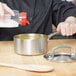 A person pouring yellow liquid into a Vollrath stainless steel sauce pan.