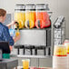 A woman pouring Carnival King Mango Slushy concentrate into a machine.