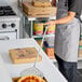 A stainless steel round perforated pizza peel with a long handle being used in a commercial kitchen.