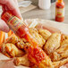 A hand pouring Marie Sharp's Smokin' Marie Habanero hot sauce onto a chicken wing.