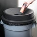 A hand pouring coffee from a cup into a 32 gallon black funnel top trash can.