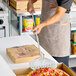 A round stainless steel perforated pizza peel with a long handle being used to serve a pepperoni pizza.