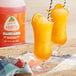 A glass of Jarritos Mandarin Slushy with a straw next to a bottle of Jarritos Mandarin Slushy.