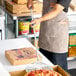 A round perforated stainless steel pizza peel with a long handle being used to transfer a pizza.
