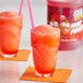 A glass of Jolly Rancher fruit punch slushy with a straw and an orange slice.
