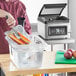 A woman using a Galaxy sous vide machine to prepare a large container of vegetables.