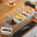 A person using a Choice stainless steel condiment bar to put fruit in a container.