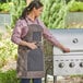 A woman wearing a Backyard Pro Smoke heavy-duty canvas grilling apron and using tongs to grill.