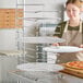A woman in a kitchen apron holding a pizza on a GI Metal pizza rack.