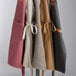 Acopa Hazleton mocha canvas restaurant aprons hanging on a rack.