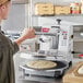 A man using an Estella manual clamshell pizza dough press to make a pizza.
