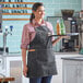 A woman wearing an Acopa Hazleton black canvas bib apron holding a tray with bottles of beverage.