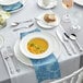 A table with a bowl of soup and Acopa Ophelia stainless steel butter knives and spoons.
