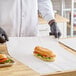 A sheet of newsprint sandwich wrap paper being used to wrap a sub sandwich on a wooden counter.