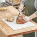 A person cutting a loaf of bread on a white polyethylene cutting board.