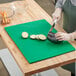 A woman cutting eggplant on a green Choice cutting board.