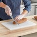 A person cutting a loaf of bread with a knife on a white polyethylene cutting board.