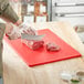 A person cutting meat on a red Choice cutting board.