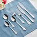 An Acopa stainless steel dinner knife and spoon on a blue cloth.