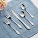 Acopa Swirl 18/8 stainless steel flatware on a blue cloth with a knife and spoon.