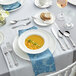 An outdoor table set with a bowl of soup, bread, and Acopa Ophelia stainless steel spoons.