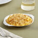 A stainless steel round au gratin dish filled with macaroni and cheese on a table with a fork.