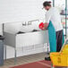 A man in a blue uniform cleaning a Regency stainless steel utility sink.