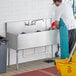 A man in a blue apron washing a Regency stainless steel utility sink.