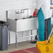 A man in a blue uniform washing a Regency stainless steel utility sink.