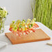 An Acopa dark brown wood skewer holder with shrimp and fruit skewers on a plate.