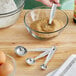 A person using a Choice stainless steel measuring spoon to scoop brown sugar into a bowl.