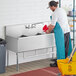 A man in a blue uniform pouring water into a Regency stainless steel utility sink.