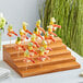 An Acopa Mesa dark brown wood skewer holder with shrimp skewers on it.