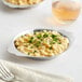 A Choice stainless steel round au gratin dish with macaroni and cheese on a plate with a fork.