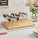 An Acopa natural wood skewer holder with cake pops on it on a table in a bakery.