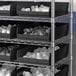 A metal shelving unit with black Regency shelf bins holding white containers.