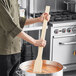 A person stirring a pot of soup with a Choice 36" Wood Paddle.