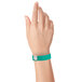 A close-up of a hand holding a teal Carnival King wristband with a silver clasp.