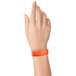 A hand holding a coral red Carnival King wristband.