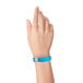 A person's hand with a Carnival King neon blue disposable plastic wristband.