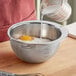 A person pouring milk into a stainless steel bowl of flour.