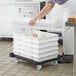 A woman putting food into a stack of white plastic Baker's Mark dough proofing containers.