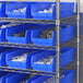 A blue Regency shelf bin on a metal shelf with grey objects inside.